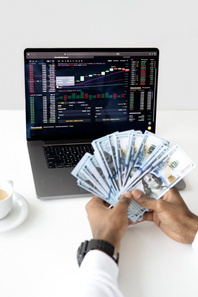 Hands holding cash in front of a laptop displaying stock market data, symbolizing financial growth and investment.
